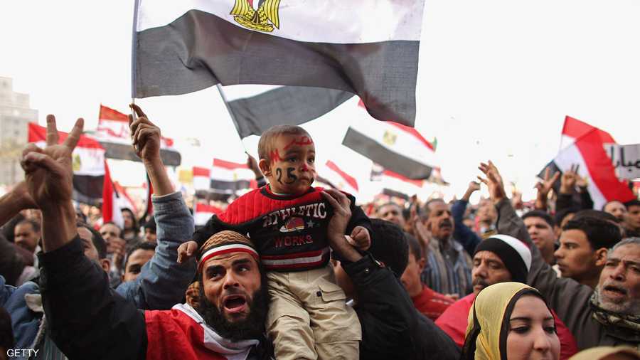 رجل يحمل طفله ويلوح بعلامة النصر في ميدان التحرير