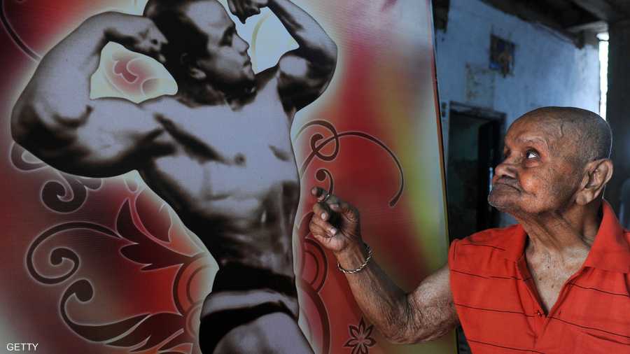 مانوهار يقف أمام ملصق لصورته عندما فاز بلقب بطولة الكون لكمال الأجسام عام 1952