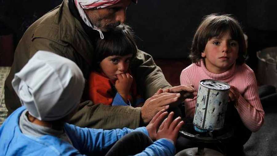 أطفال سوريون يحيطون بموقد يحاولون الحصول على الدفئ داخل خيمتهم في مخيم الزعتري بالأردن