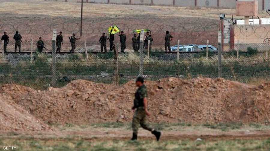 مقاتلون أكراد يلوحون بعلمهم.. وعلى الجانب الآخر جندي تركي يترقب
