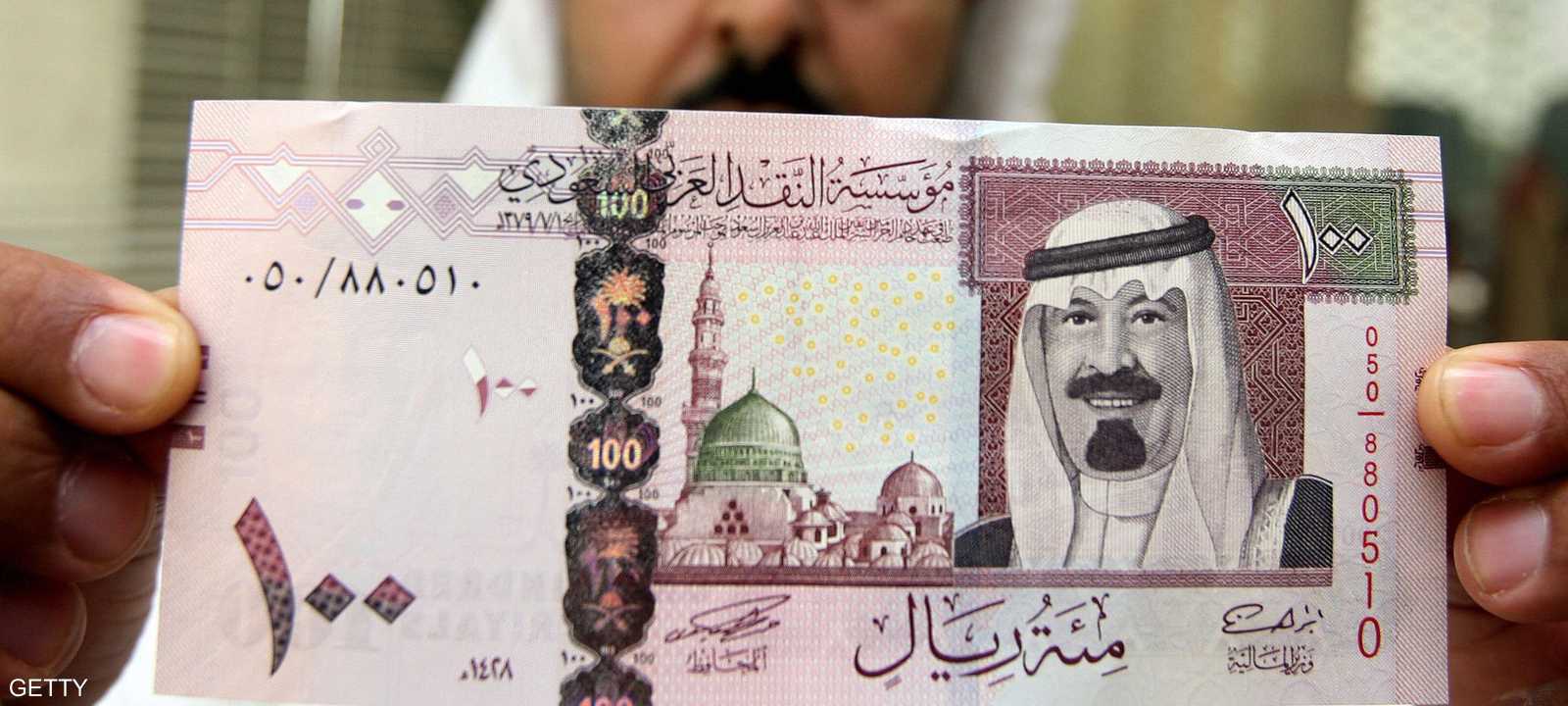 موظف بنكي يستعرض ورقة نقدية فئة 100 ريال سعودي في الرياض - أرشيف
