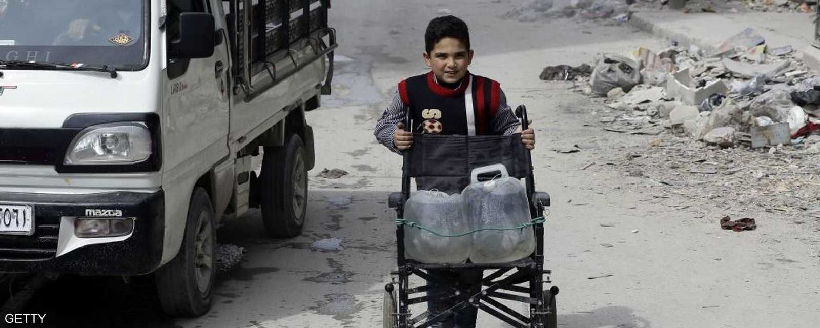 طفل سوري ينقل الماء بواسطة الكرسي المتحرك