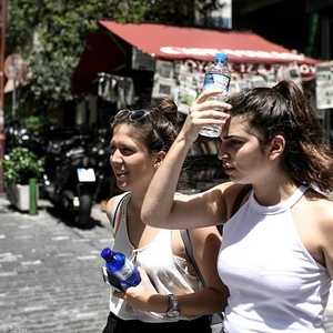 شابة يونانية تقاوم الحر بقنينة ماء