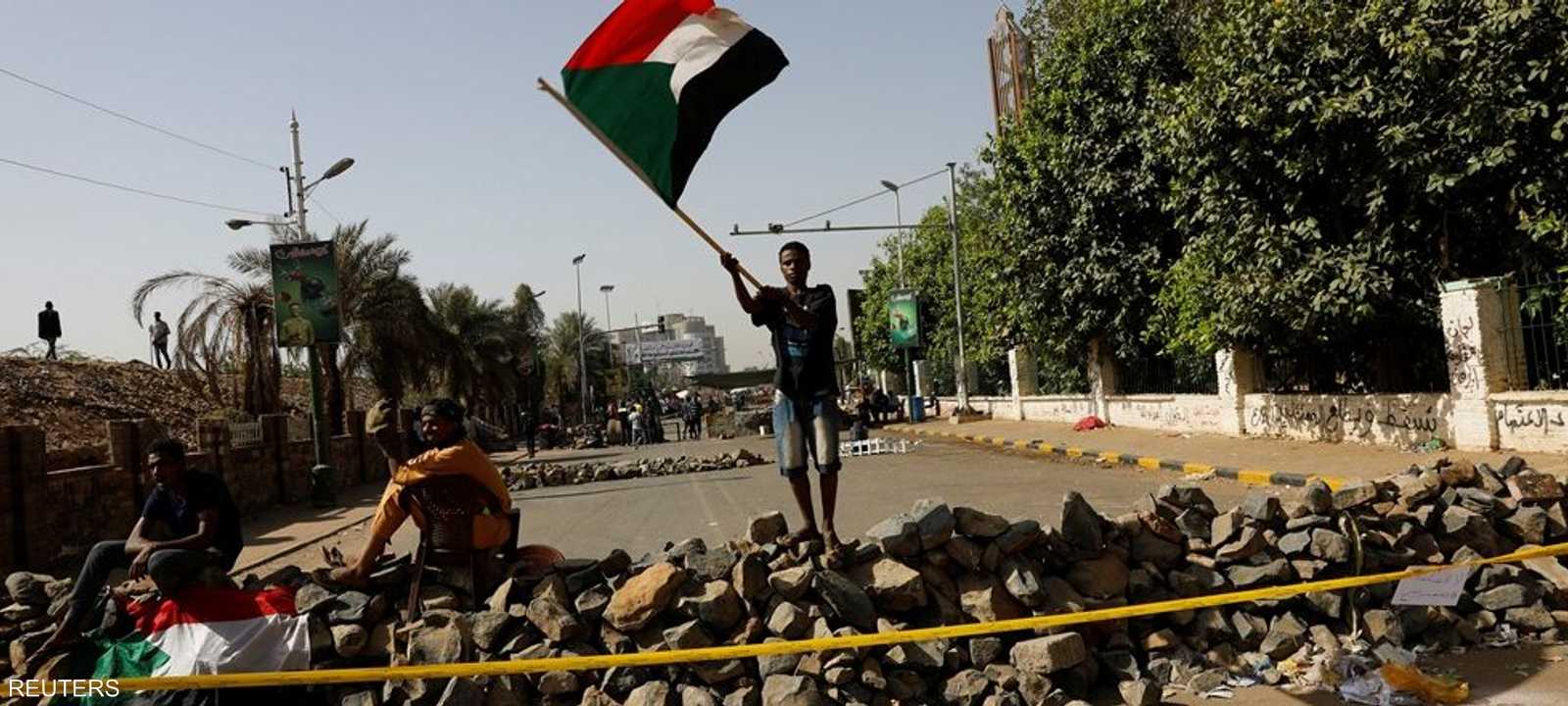 متظاهر سوداني يرفع علم بلاده أمام عوائق أمام موقع الاعتصام.