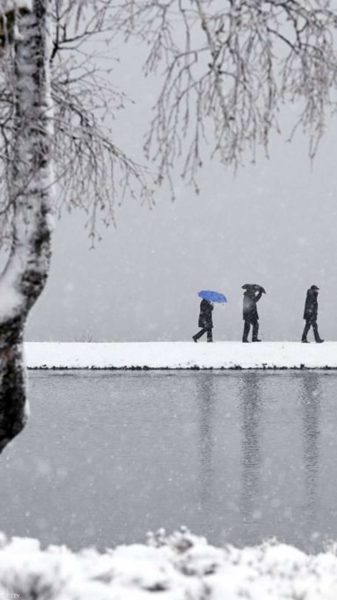 بعض السكان في ألمانيا يسيرون على ضفاف بحيرة وسط الثلوج التي كست كل شيء باللون الأبيض.