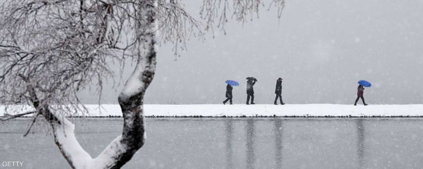 بعض السكان في ألمانيا يسيرون على ضفاف بحيرة وسط الثلوج التي كست كل شيء باللون الأبيض.