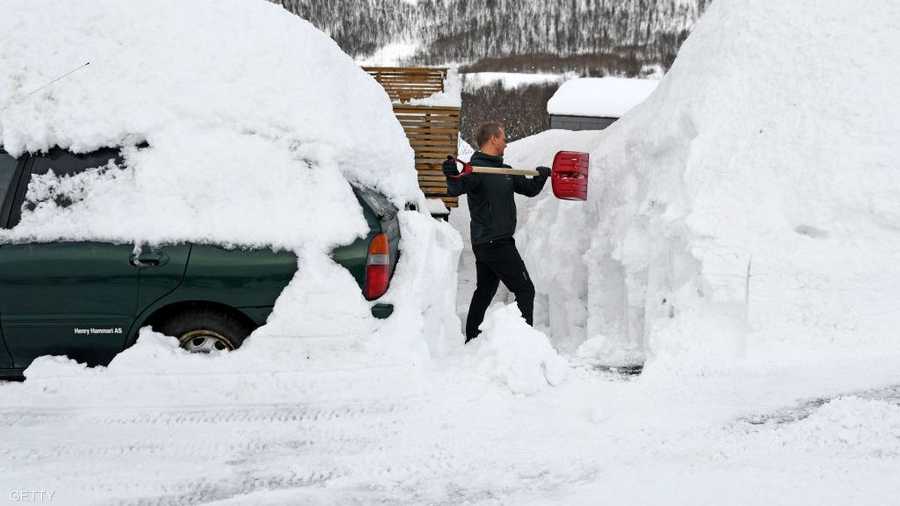 رجل نرويجي يزيح ما تراكم من ثلوج أمام منزل بينما تبدو سيارته مغمورة بالثلوج.