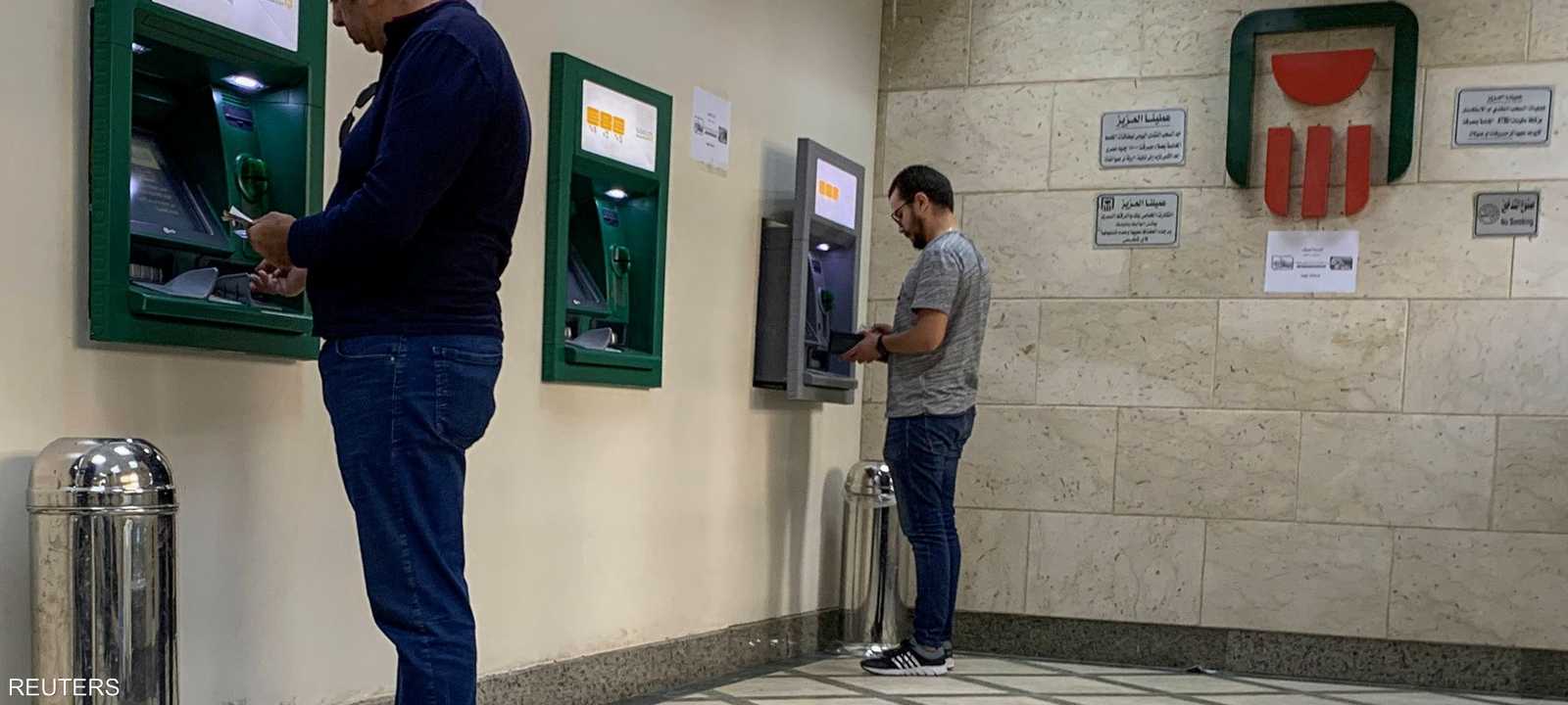 شخصان يسحبان أموالا من ماكينات الصراف الآلي.