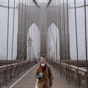 سيدة ترتدي الكمامة وتقف وحيدة على جسر بروكلين في نيويورك.