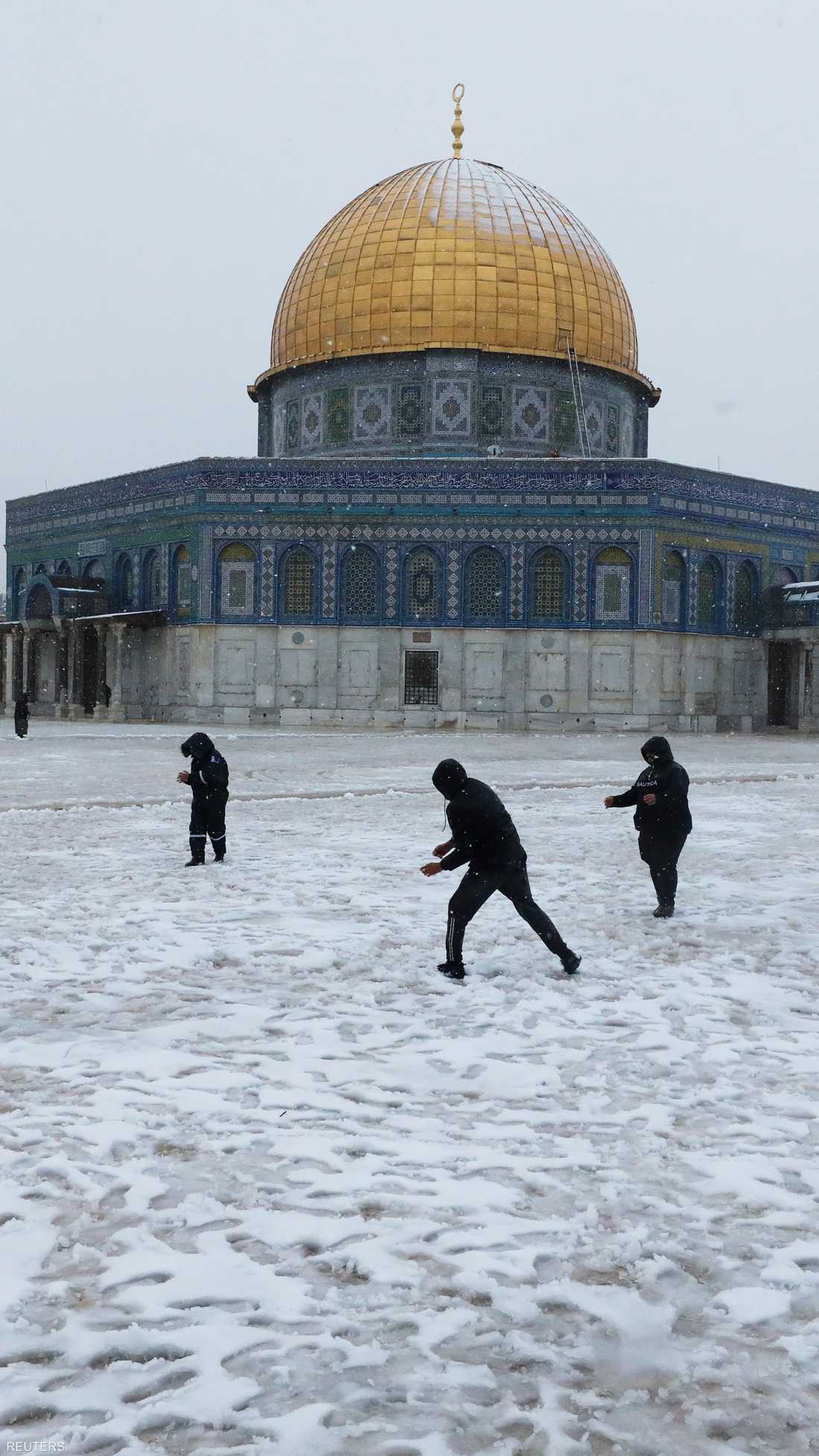 يلعب الناس بأكوام الثلج بجانب قبة الصخرة في القدس