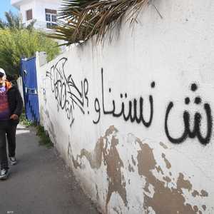تونسيون يمرون جانب حائط وعبارة تندد بالميزانية في تونس