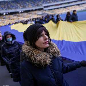 أوكرانيون وأوكرانيات يمسكن بعلم ضخم في استاد كييف، الأربعاء.