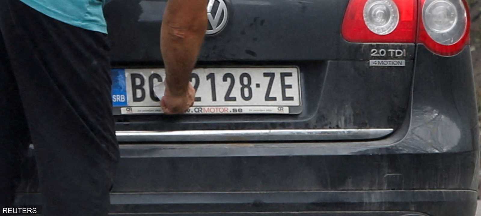 سائق يزيل ملصقًا يغطي العلامة الوطنية على لوحة سيارته