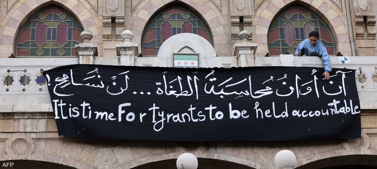 رجل يقف خلف لافتة تطالب بمحاسبة مرتكبي الجرائم في سوريا