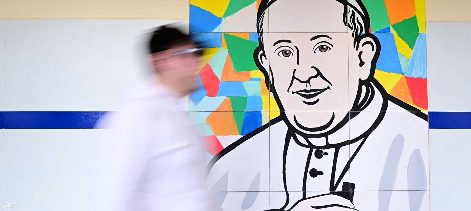 رجل يمشي أمام صورة للبابا في مستشفى جيميلي الجامعي