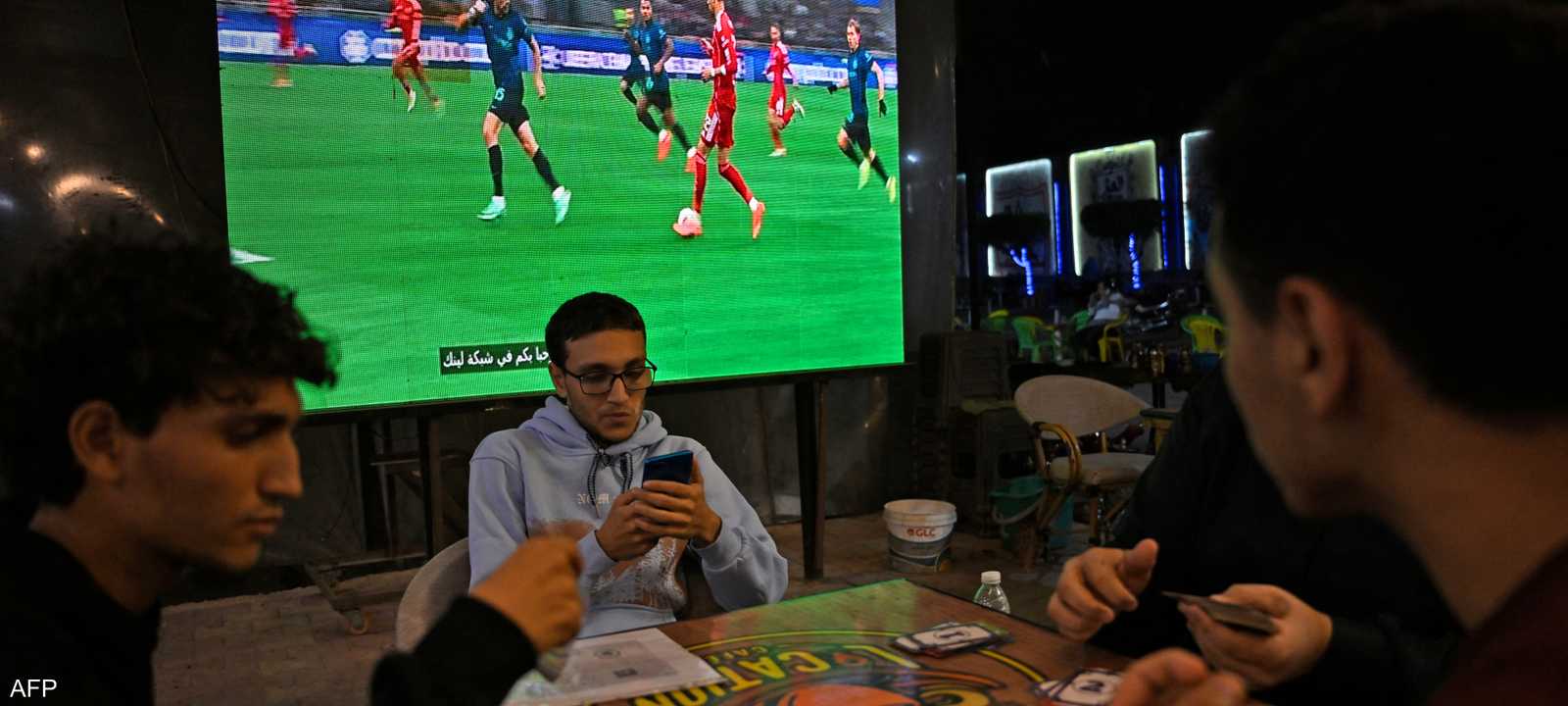 يجلس الزبائن في المقهى بعضهم منشغل أثناء مباراة ليفربول