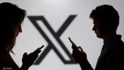شخصان يحملان هواتف ذكية أمام شعار منصة إكس في صورة تعبيرية