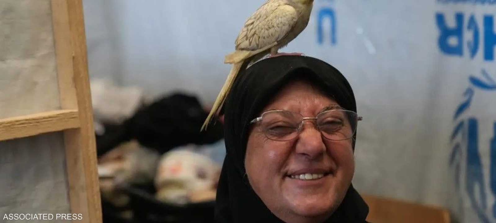تجلس علوية داخل غرفتها المؤقتة ويقف ببغاؤها فوق رأسها