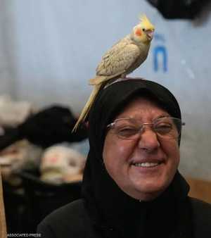 تجلس علوية داخل غرفتها المؤقتة ويقف ببغاؤها فوق رأسها