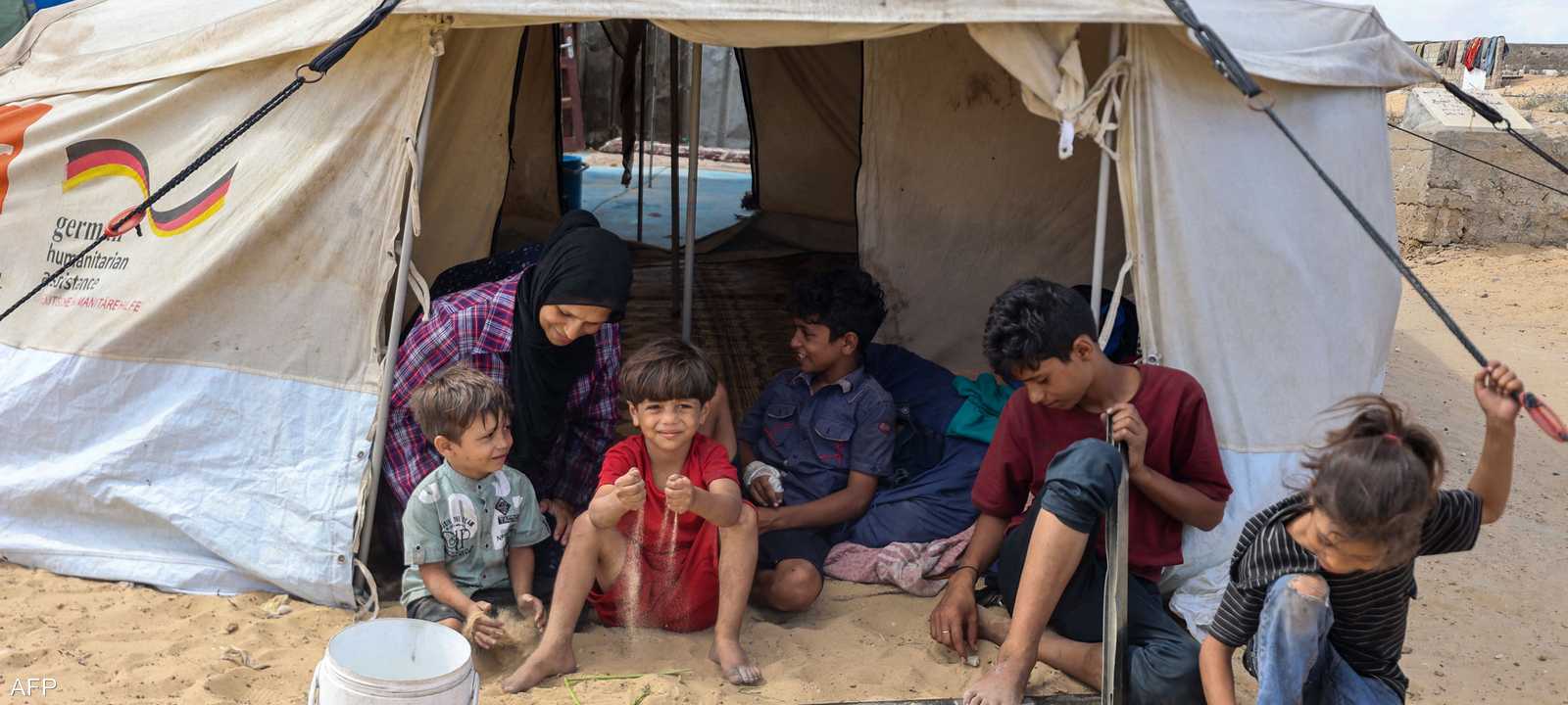 أم تجلس مع أطفالها في خيمة نُصبت وسط مقبرة في خان يونس